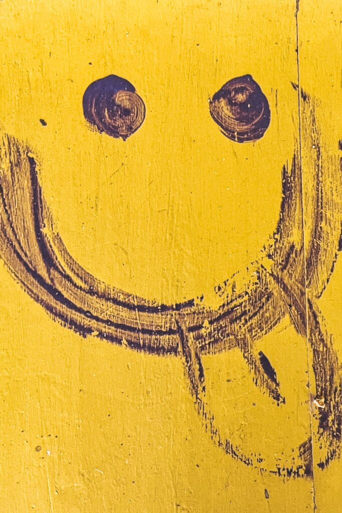Close-up of a funny hand-drawn smiley face on a yellow wall with texture.